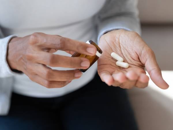 Person tipping two tablets from a pill bottle into their hand