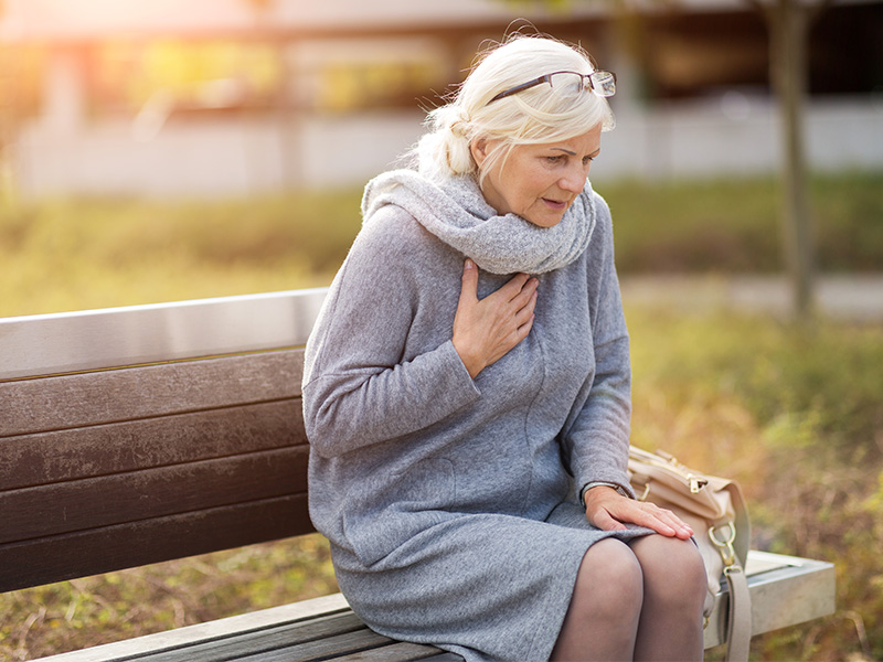 Mature woman sitting on bench clutching chest