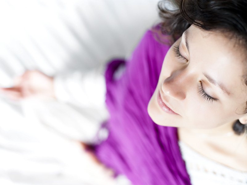 woman wearing purple cardigan sitting cross-legged meditating