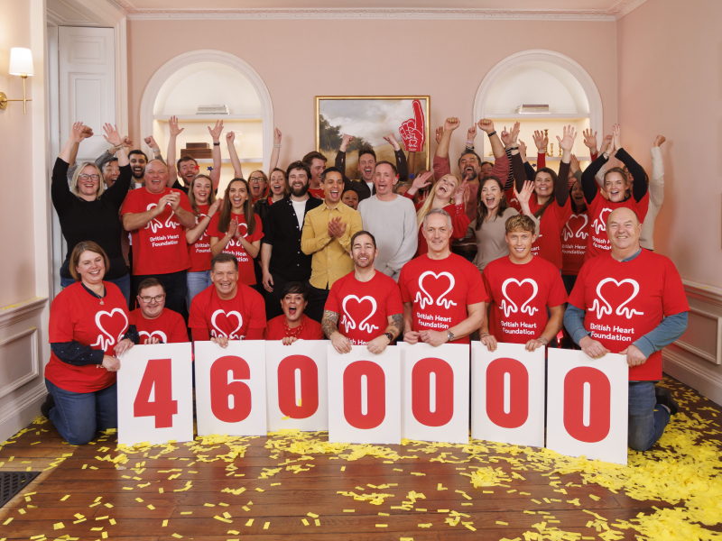 A team wearing red BHF t-shirts are celebrating and holding a fundraising total on cards. It reads £4,600,000.