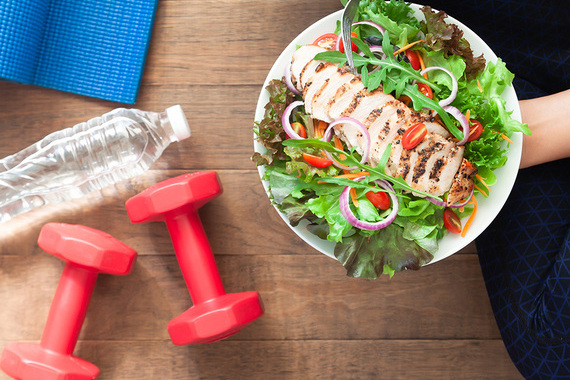 A bowl of chicken salad with a bottle of water and some red weights
