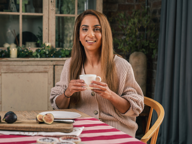 Neena, sat at a table holding a mug
