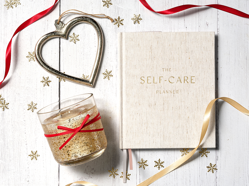 A candle and self-care journal laid out on a table with some stars, a heart and a red ribbon