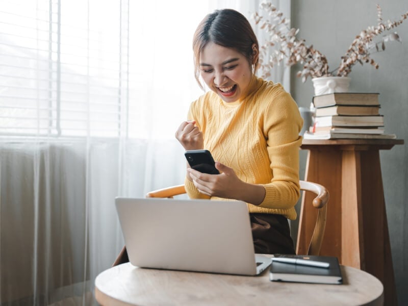 A person looking at their phone and smiling, having received some good news