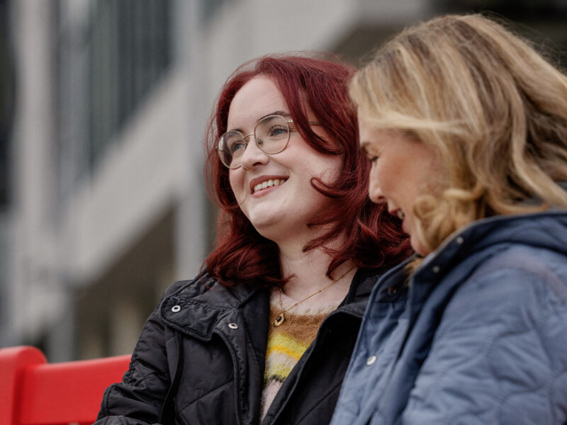 Caoimhe, sitting on a red bench with a family member.