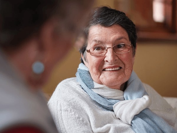 An older adult smiles at her family member across the room