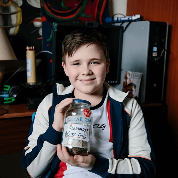 A boy holds up coins and notes in a swear jar ready to donate to BHF