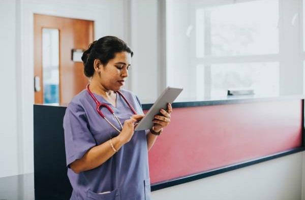 an Asian female doctor using a tablet computer as she stands in the reception area of a hospital