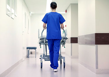 Nurse walking down a corridor pushing a bed