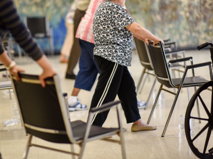 A cardiac rehabilitation class showing  people practising exercises while holding onto a chair.