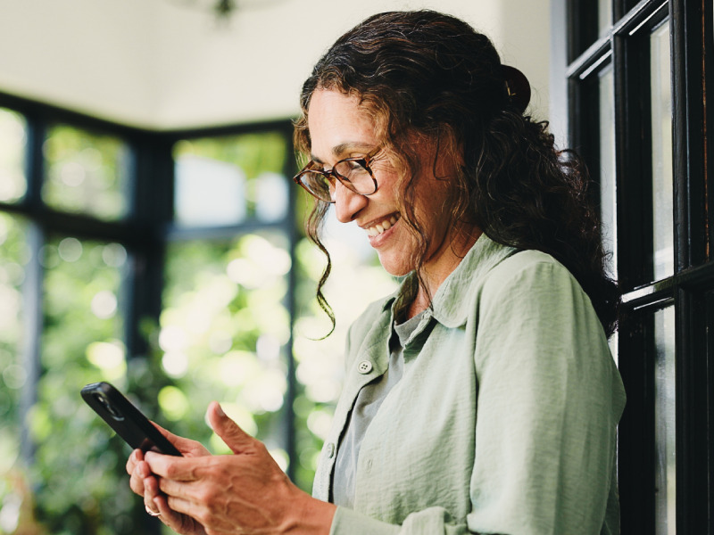 A woman using a smartphone and leaning against a door in her home