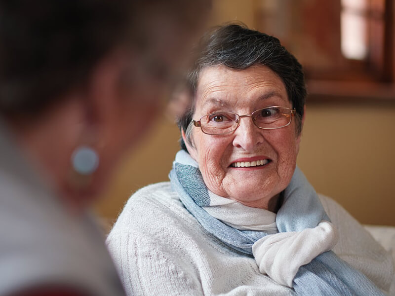 An elderly woman is smiling at a relative