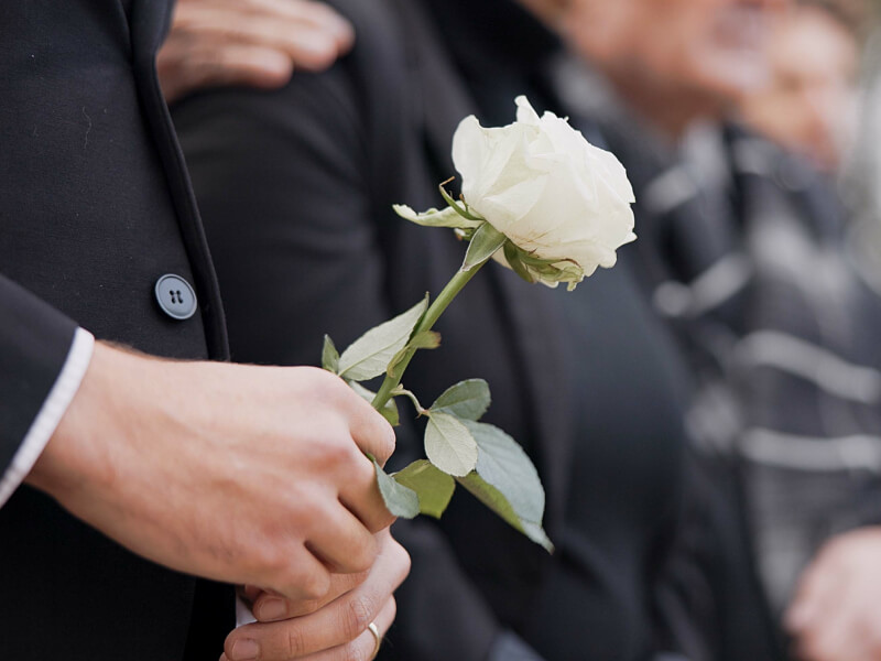 Hands holding a white rose at a funeral
