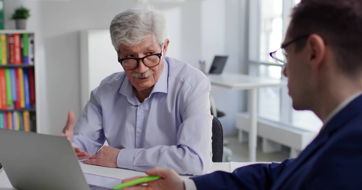 A man sits at a desk speaking with his solicitor, who is reviewing documents..