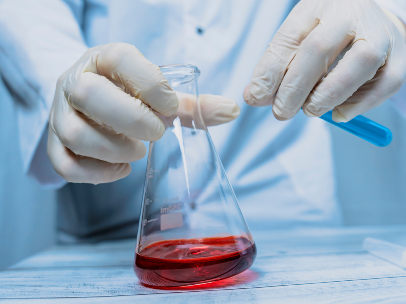 A scientist holding a test tube with a red substance inside.