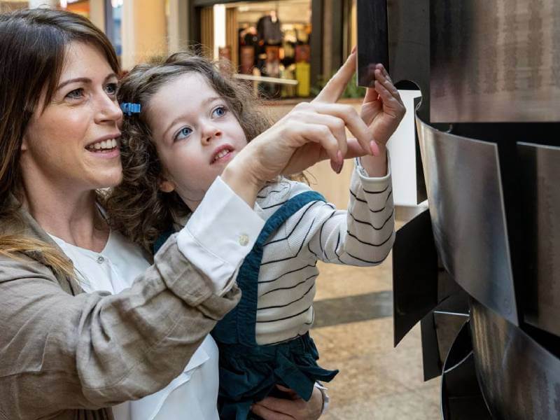 Woman holding her child and looking at an engraving on the Heart of Steel sculpture