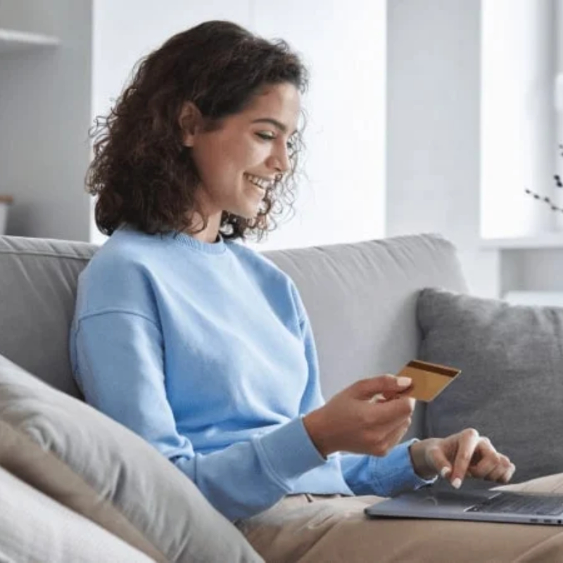 A woman holding a bank card is donating on a laptop.