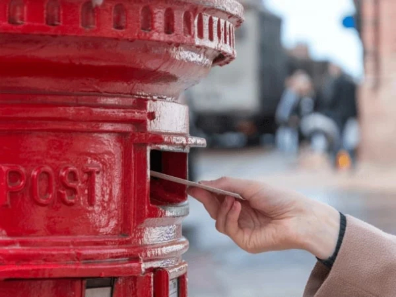 A hand posting a letter in a red letterbox.