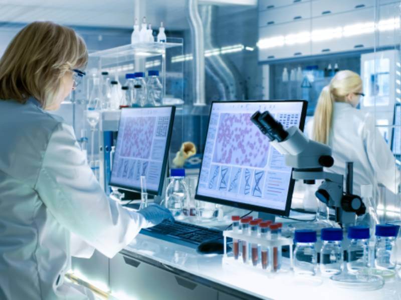 Researcher working in a laboratory with computer screens and other equipment.