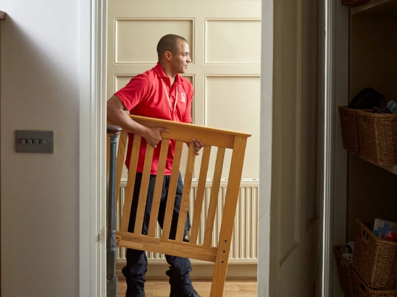 A person wearing a BHF shirt is moving a bedframe during a house clearance.