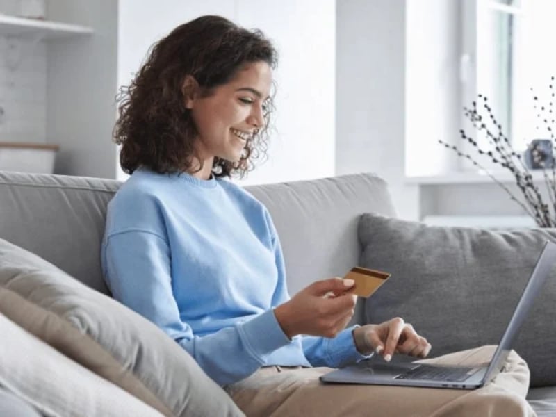 A woman holding a bank card is donating on a laptop.