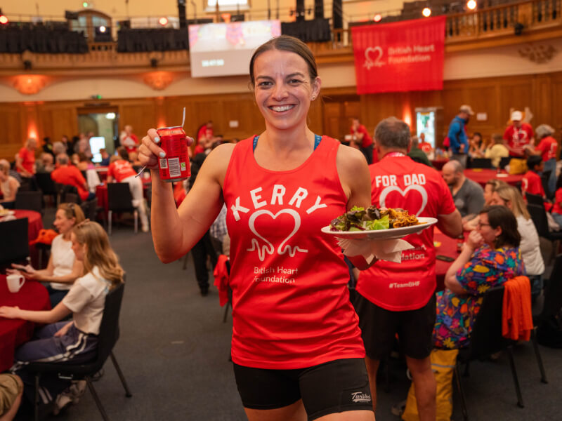 BHF runner in red singlet holding a plate of food and a soda can