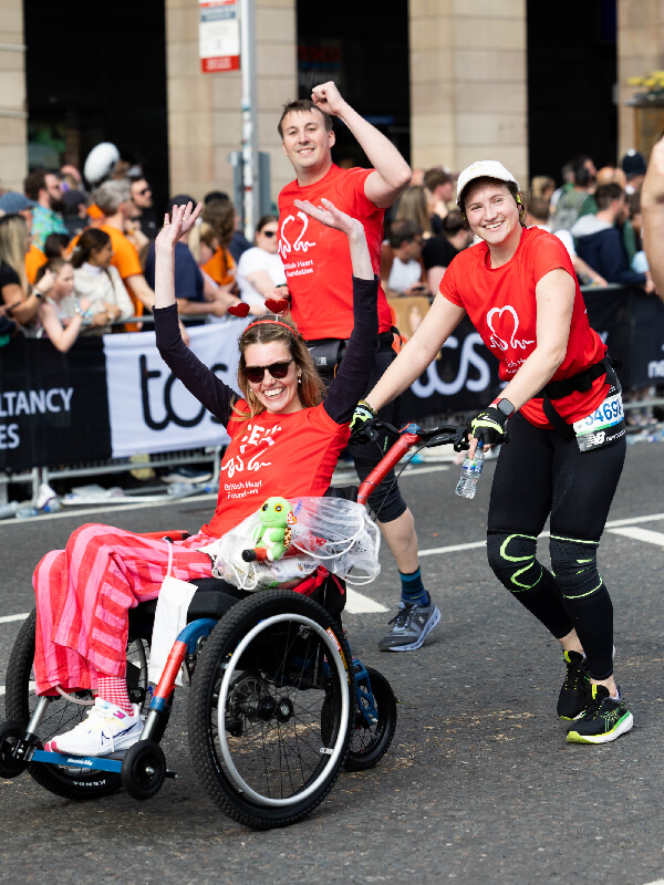 Two BHF supporters cheering as they push a BHF supporter in a wheelchair 