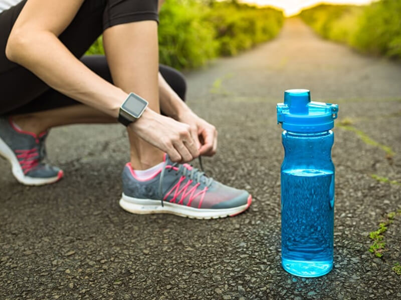 A runner tying their laces next to a bottle of water 