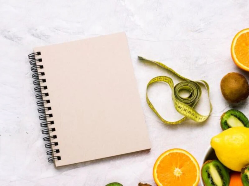 A diary next to a table of fruit and a measuring tape