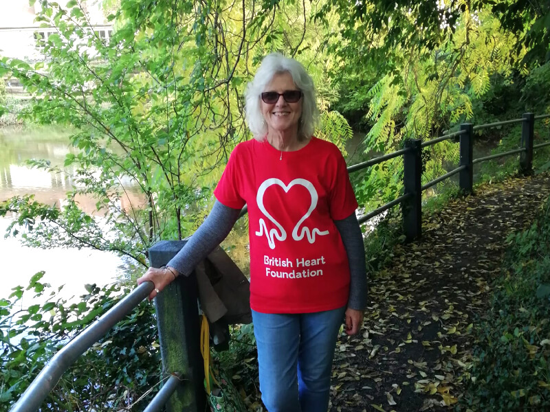 A photograph of Sue, walking through trees near a lake.