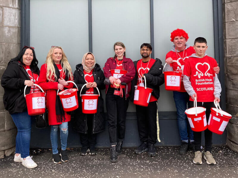 Seven members of a fundraising group are wearing BHF t-shirts and holding collection buckets.
