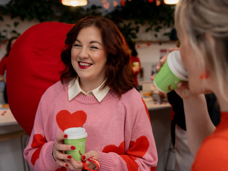 A woman in a heart jumper having coffee with colleagues