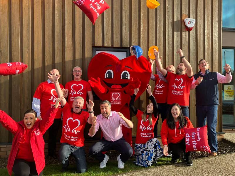 Group of colleagues in red BHF t-shirts posing with Hearty, the BHF mascott, and throwing red cushions in the air