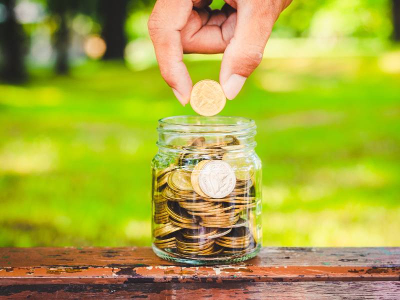 A hand placing a coin into a jar full of coins