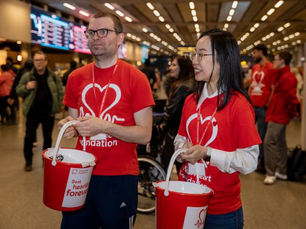 Two fundraisers wearing bhf t-shirts and holding buckets in a train station