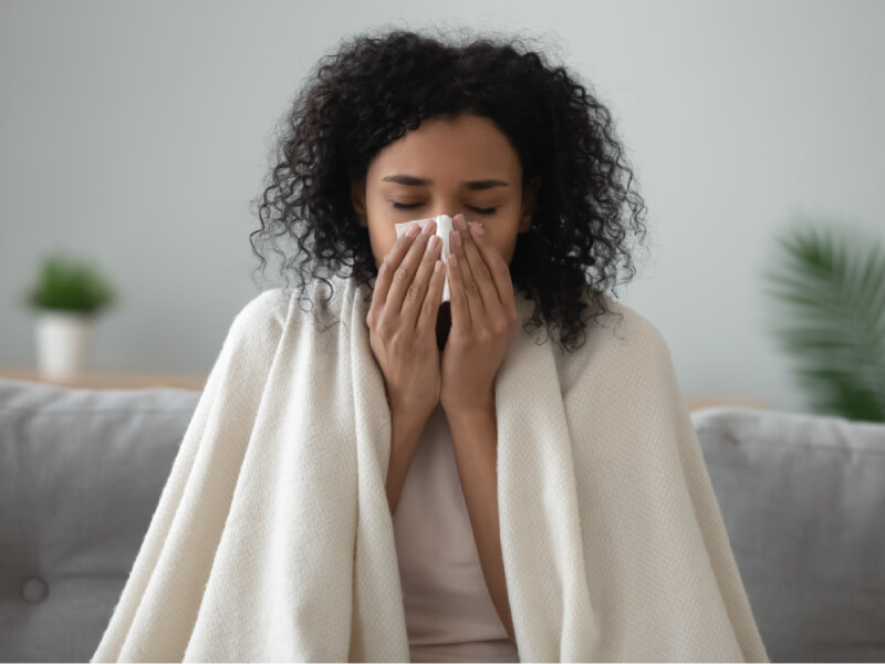 A black woman with a blanket on her shoulders is covering her nose with a tissue