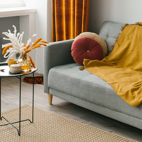 Grey sofa with a yellow throw on it, with a metal coffee table and beige rug