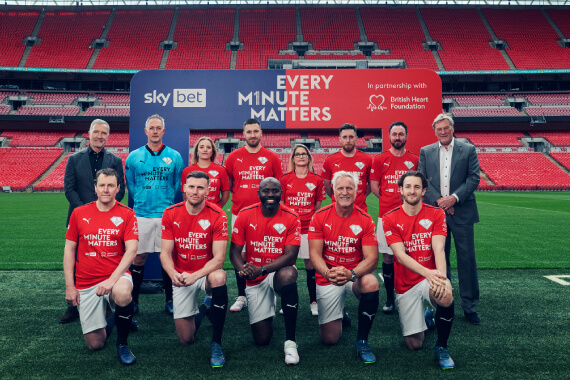 Footballers posing on football pitch with sign in the background saying 'Every Minute Matters' with Sky Bet and BHF logos.