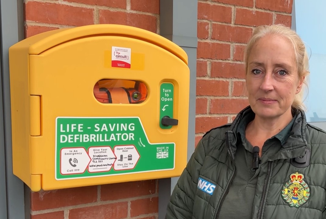 a female paramedic standing next to a defibrillator on an outside wall