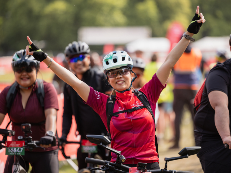A London to Brighton bike rider with their hands in the air smiling
