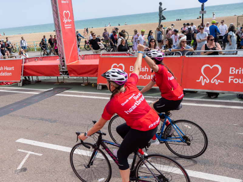 Two bike riders holding each others hands as they approach the finish line