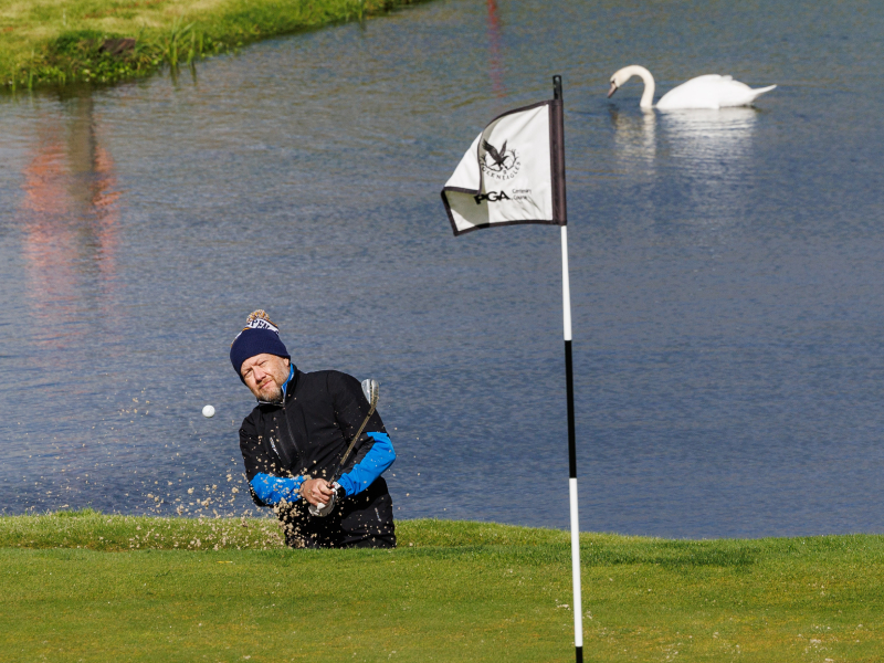 A man playing golf hitting a ball out of the bunker and onto the green