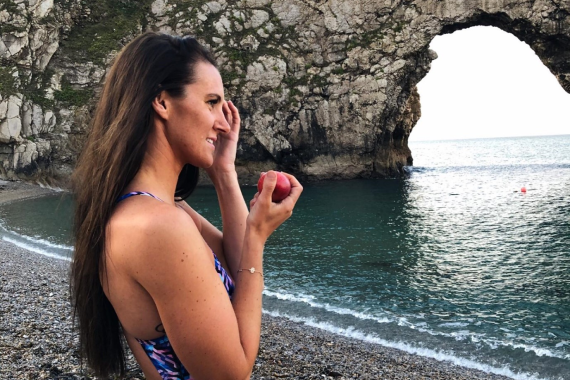Woman in a swimsuit holding a Jazz Apple on the seafront.