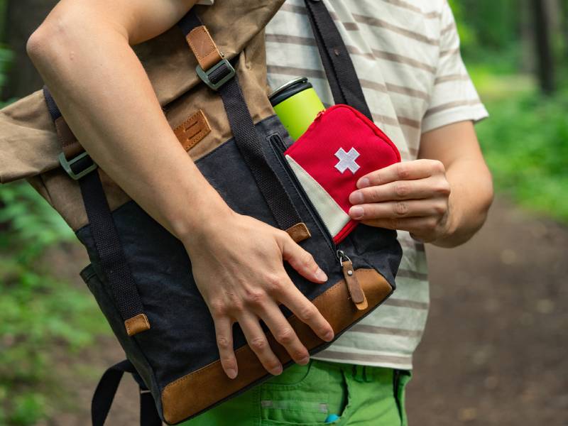 A person pulls a First Aid kit out of their backpack.