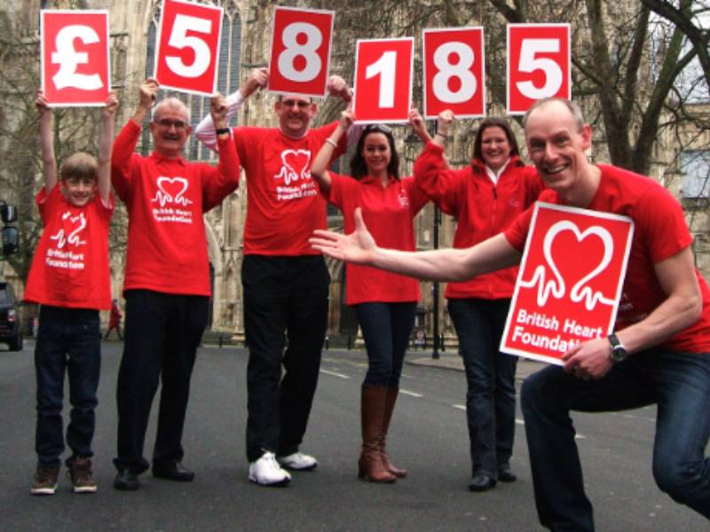 A group of BHF volunteers. Above their heads they are holding a sign that reads £58,185.