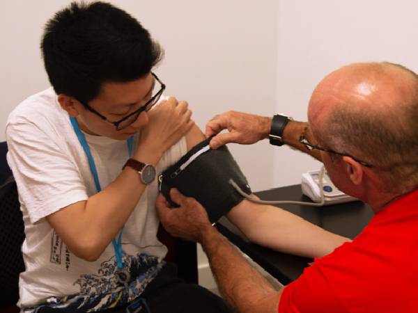 A male Health at Work adviser using a blood pressure monitor on a man of Asian heritage 