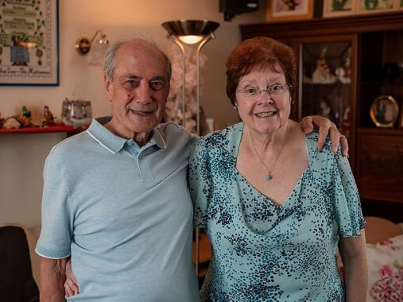 Two elderly people with each other's arms over their shoulders