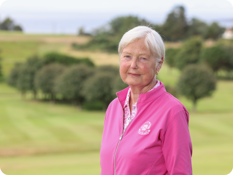 Valerie McIlveen in a pink jacket standing outdoors, with a green landscape and trees in the background.