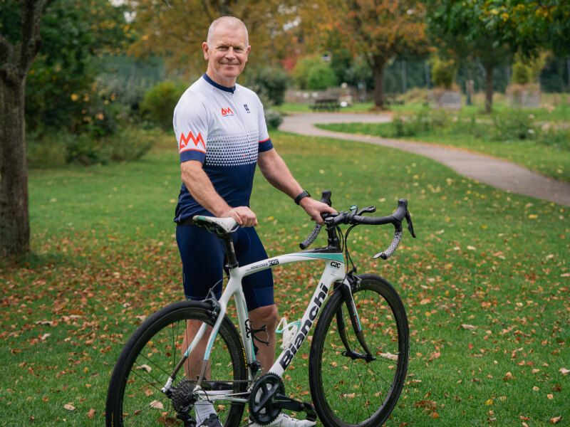 A man smiling standing next to his bike in the park