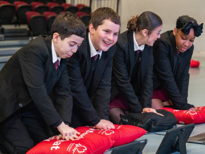 4 school students practising CPR compressions on cushions